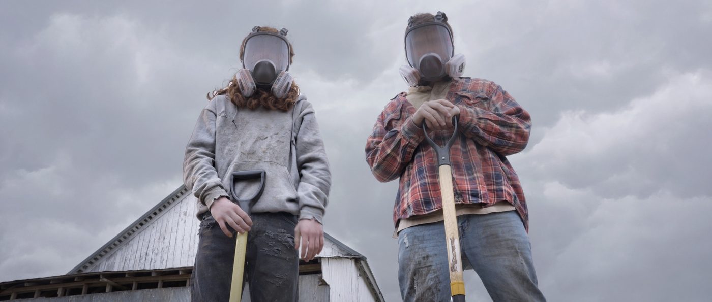 Samuel and Jude stand masked against a stormy sky, holding shovels.